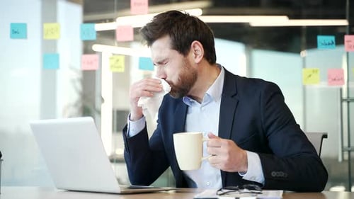 Man Blowing Nose While Working at Office Desk