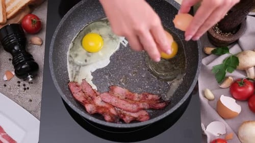 Cracking Eggs Into Skillet with Bacon for Breakfast