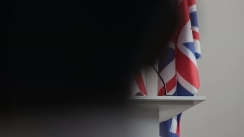 Man Speaking Behind a Podium with Flags
