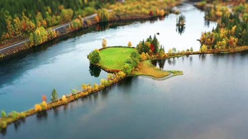 Aerial view of a small, vibrant green island encircled by calm water, with autumn trees lining the s