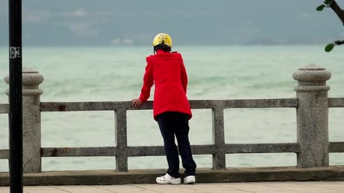 Rückansicht einer nicht wiederzuerkennenden einsamen Frau oder eines Mannes, die auf einem Damm in der Nähe eines Betonzauns stehen und