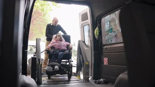 Caregiver Assisting Man with Disability in Wheelchair Onto Accessible Van Lift