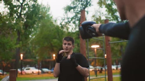 Male Athlete Works on Punches with Coach in Evening Park Young Martial Artist Focuses on Defensive