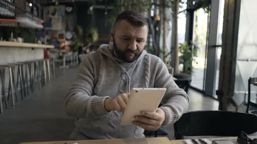 Young man browsing online with tablet computer inside bright cafe in the city