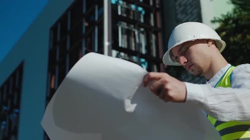 ein männlicher Architekt, ein Baumeister mit einem weißen Schutzhelm und einer Arbeitsweste, schreibt Daten für den Bau auf Papier d