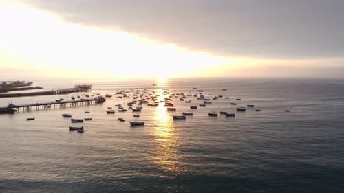 Drone video of boats anchored in ocean by a pier. Shot during sunset. The sun light hits different b