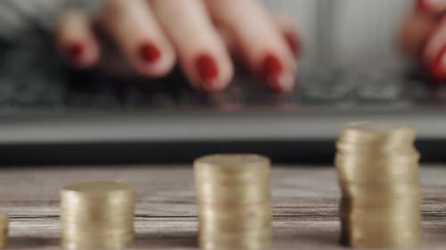 Woman Typing on Laptop with Stacks of Coins