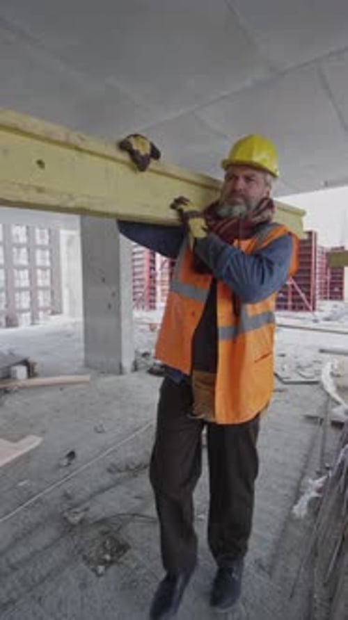 Construction Worker Carries Beam Through Building Site
