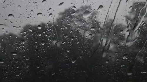 Dies ist ein Video von großen Regentropfen, die auf dem Fenster landen und dazu führen, dass sich kleine Ströme bilden und rollen