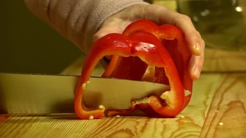 Knife cuts the red pepper in kitchen on wooden board. Close up.