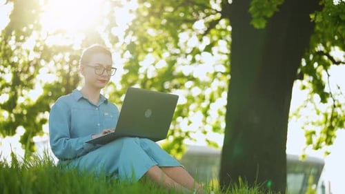 Busy Attractive Woman Working on the Laptop As Sitting on Grass in City Park
