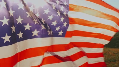 Detailed View Of American Banner Billowing Over Green Field With Sunlight Shining Through