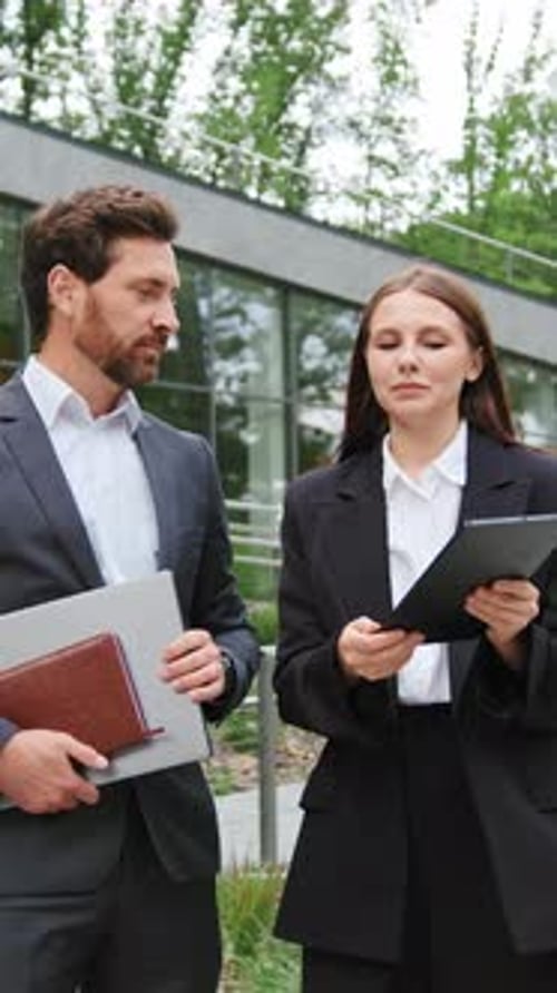 Two Business People Man and Woman in Formal Attire Stand Outside Modern Office Building Discuss