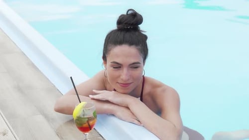 Charming Young Woman Unwinding By the Pool with a Refreshing Cocktail