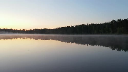 Flying over lake at dawn. Early morning mist above water. Beautiful sunrise, clear sky, calm water a