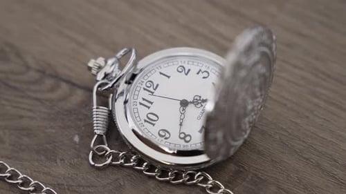 Nahaufnahme einer offenen silbernen Taschenuhr, die auf einer Holzoberfläche liegt und 8:00 Uhr anzeigt