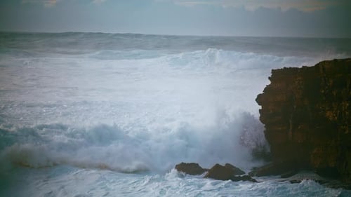 Dramatic stormy sea waves crashing against rocky cliff coastline in slow motion