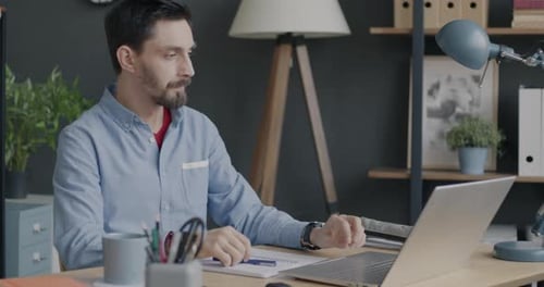 Serious Businessman Working with Laptop Typing Then Checking Smartphone Screen Indoors in Office