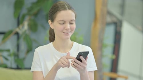 Young Woman Smiling While Using Phone Indoors
