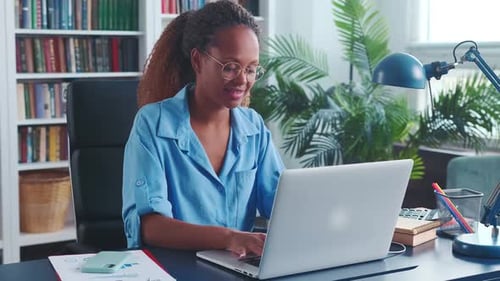 Young African American Woman Journalist Typing Article on Laptop Sits at Desk