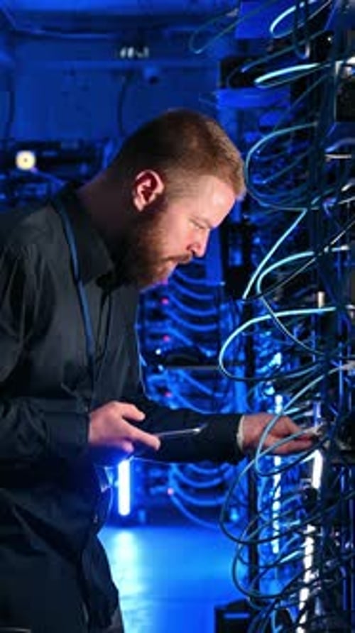 IT Professional Uses Phone in Dimly Lit Server Room