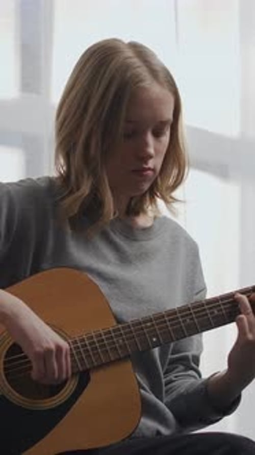 Teen Girl Plays Acoustic Guitar Indoors by Window