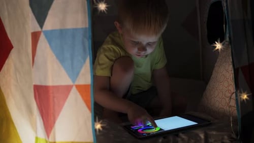 Child Plays Tablet Inside Cozy Tent at Night