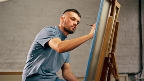 Young Artist in a Blue Tshirt in an Art Studio Working on Painting While Sitting