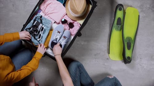 Couple packing travel essentials for summer holiday trip top view on wooden table