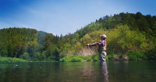 Fly fishing. Angler stands in the river and casts the fly. Fisherman fishing on fly on the calm rive