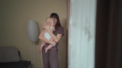A young mother holds her cute baby in her arms, gently kisses and caresses her. Mother's Day.