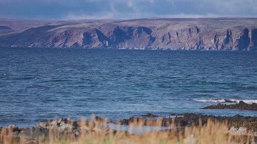 Les vagues déferlent sur la côte rocheuse. Herbe desséchée sur le rivage. La tour des montagnes à l'horizon. Parallaxe