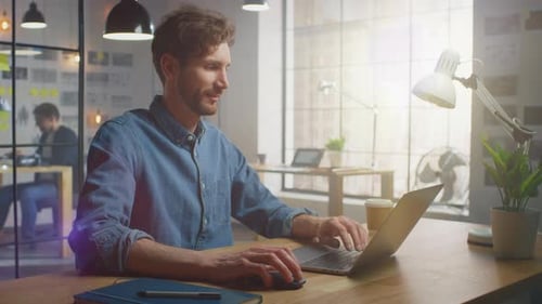 Handsome Creative Male in Jeans Shirt Works on a Laptop in His Sunny Loft Office. He Looks Cool and