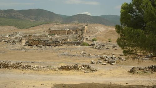 Ruínas da cidade antiga na base da montanha, grama seca e pedras espalhadas por toda parte.