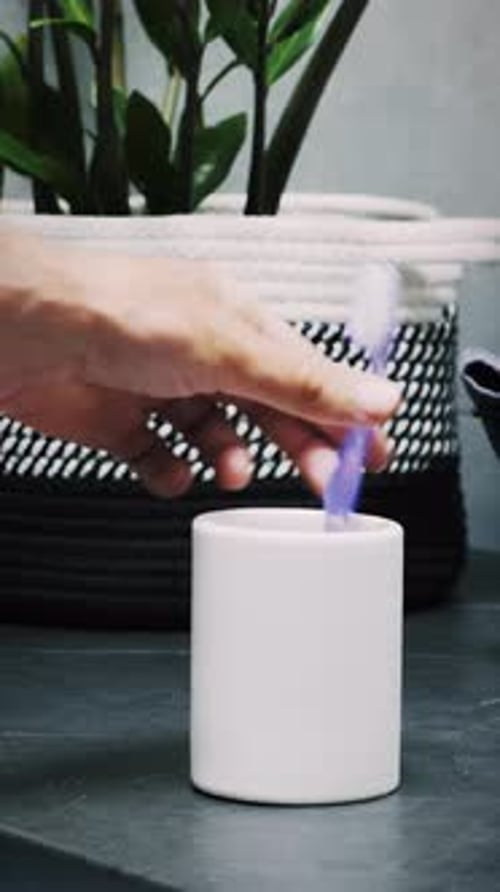 Hand putting toothbrushes in plastic cup in bathroom, close up. Vertical video