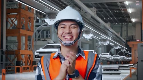 Gros plan d'un ingénieur asiatique souriant et tapant dans ses mains dans une usine de voitures électriques