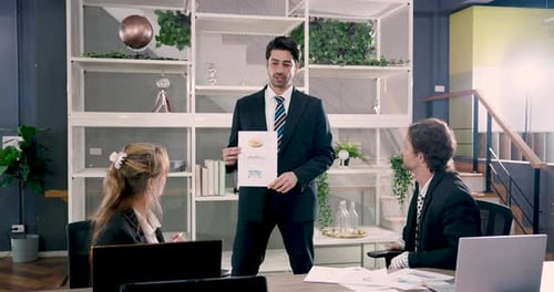 Male executive presenting colorful chart to team members during office meeting while standing confid