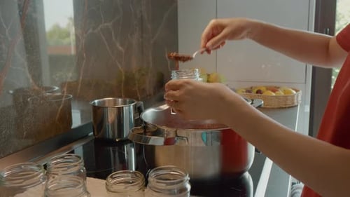 Une femme met en pot de la confiture de prunes fraîchement bouillie dans une cuisine moderne