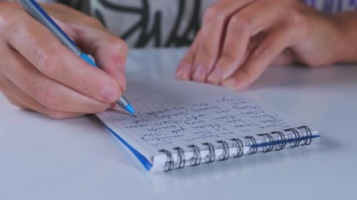 Close-up of Hands Writing in a Spiral Notebook with a Blue Pen