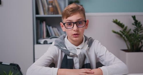 Caucasian kid having a video chat. Close up portrait little boy sit on table at home look at camera