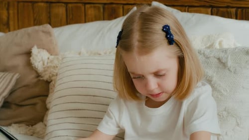 Caucasian Small Little Daughter Reading Book in Bed at Home