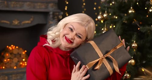 Woman Holding Christmas Gift by Decorated Tree