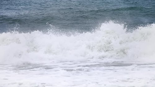 Pan of white water from a small crashing wave in slow motion in the shore with a deep dark blue ocea