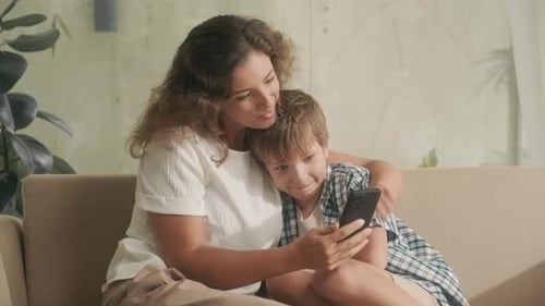 Woman and Boy Looking at Smartphone Together on Sofa