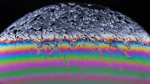 Close-up footage of the colourful surface of a soap bubble as it begins to break down