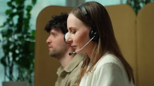 Side View of a Beautiful Young Business Woman and a Handsome Businessman Wearing Headphones Using