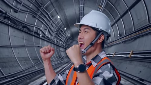 Side View Of Asian Male Engineer Screaming Goal Celebrating Working In Subway Tunnel