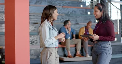 Diverse female coworkers approaching with coffee cup tablet tapping shaking hands in meeting area