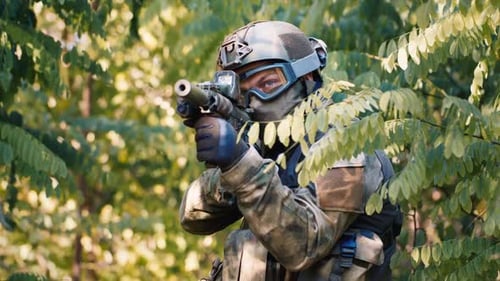 Soldier Aims Rifle in Camouflage Amongst Green Foliage
