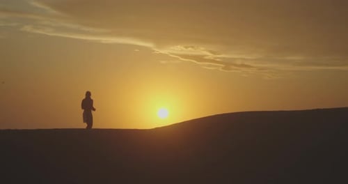 Silhouette eines Mannes, der mit einer Schlange um den Hals über Wüstensanddünen bei Sonnenuntergang in Ägypten geht.